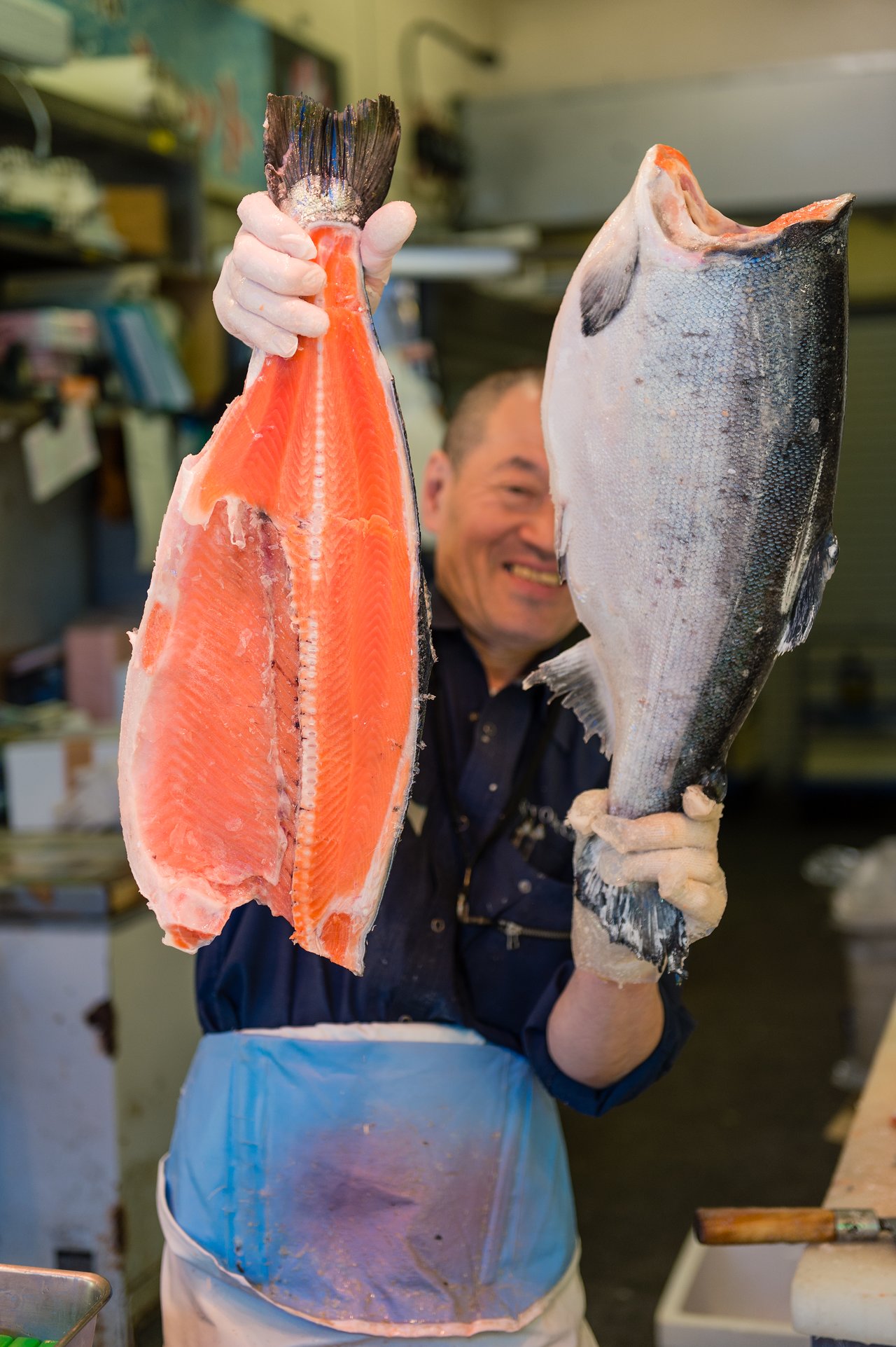A gloved fishmonger holds a frozen fish, cut in half.