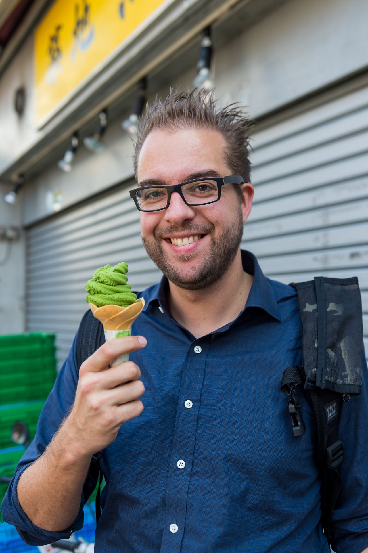 A man in glasses and a blue shirt smiles while holding a cone with green ice cream.