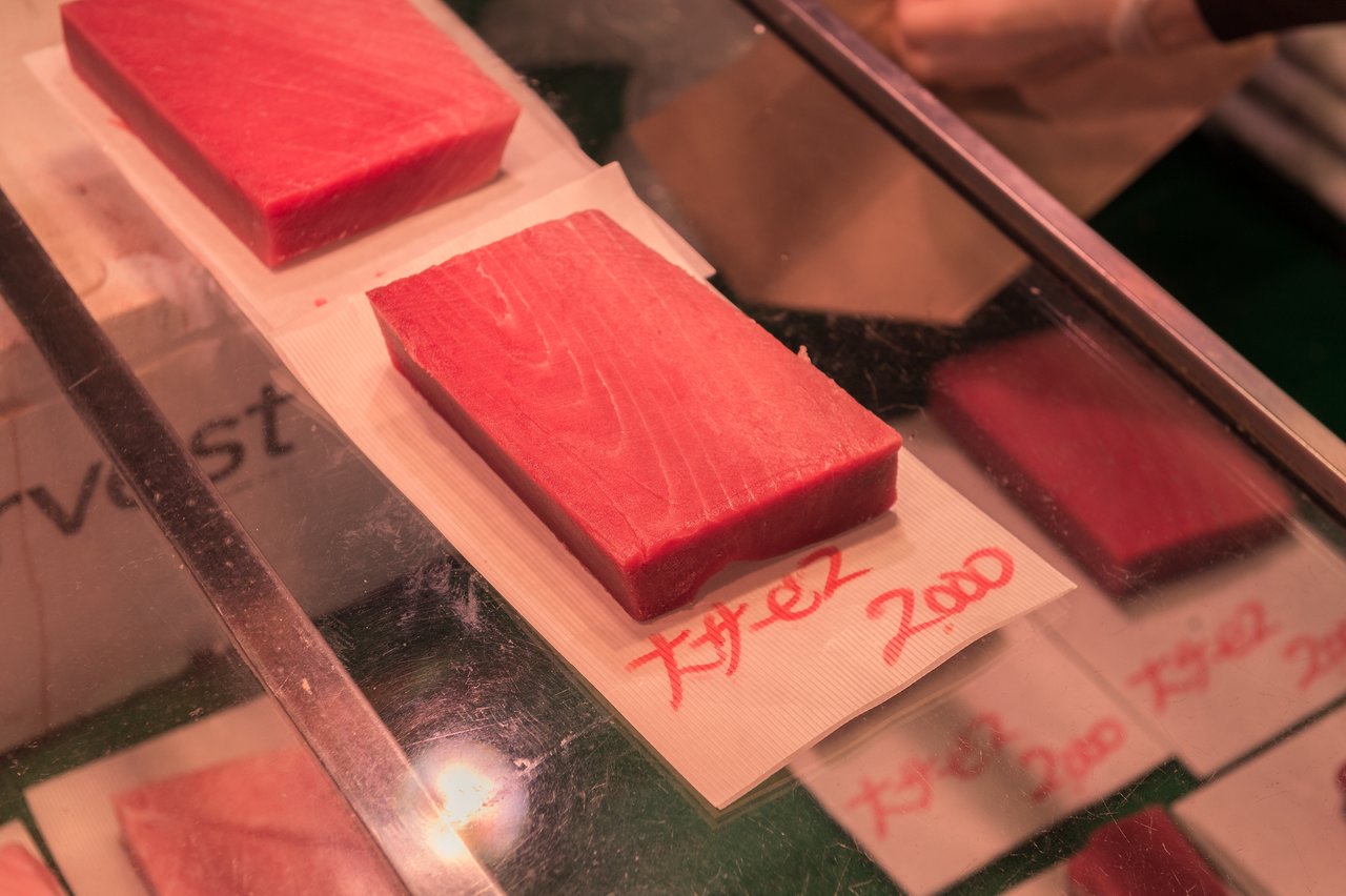 Several thick cuts of fresh tuna are displayed on a glass counter with handwritten price tags.