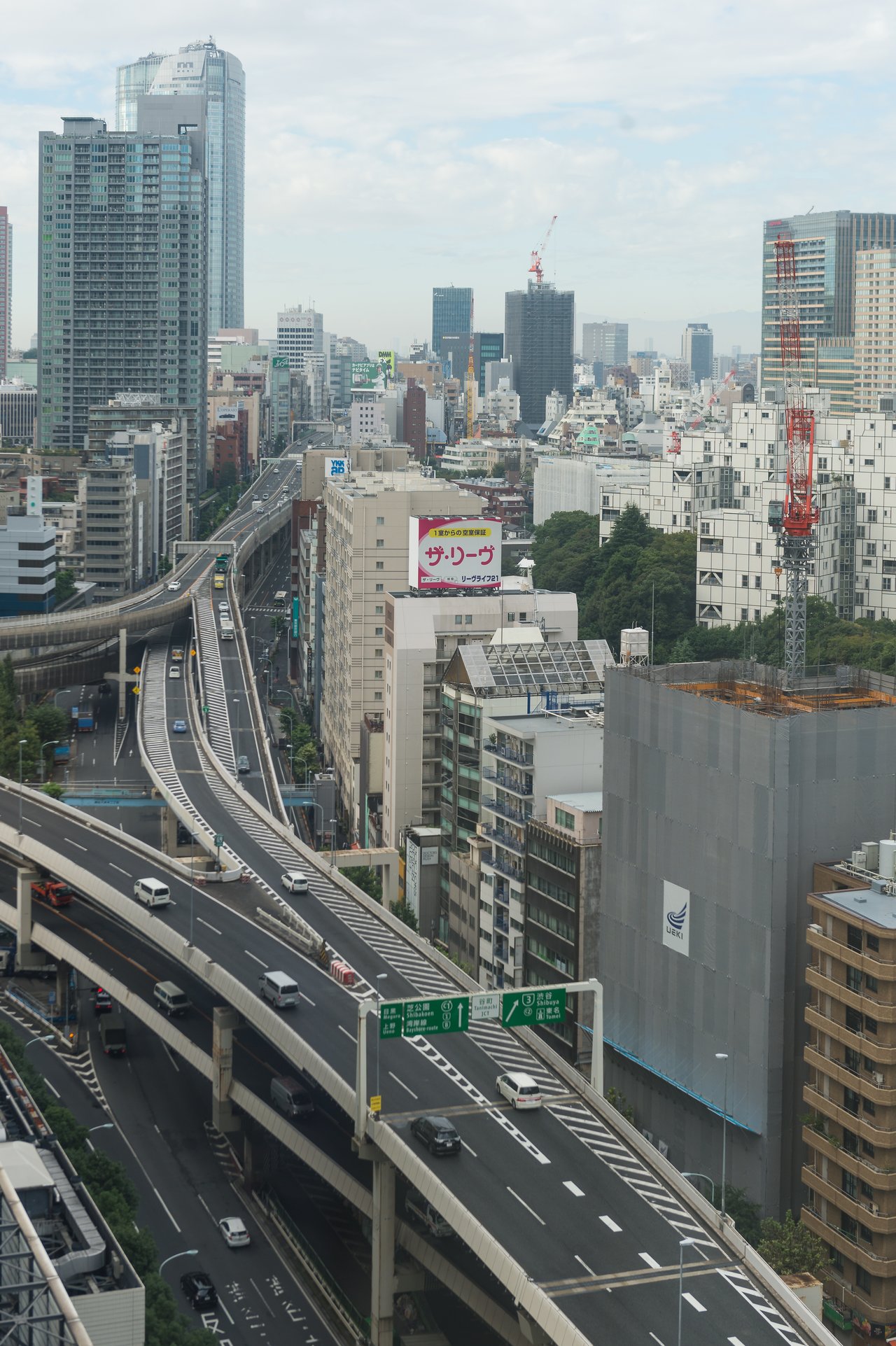 A multi-level highway with cars driving through a dense cityscape filled with tall buildings and construction cranes.