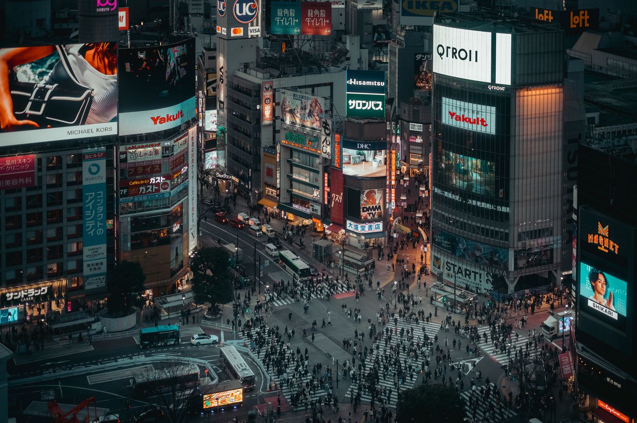 Areal view of an intersection, capturing the evening commute with pedestrians, traffic and electronic billboards.