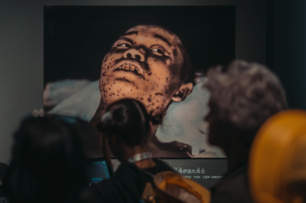 Visitors, including schoolchildren in yellow hats, look at a photograph of an injured child at the Hiroshima Peace Memorial Museum.