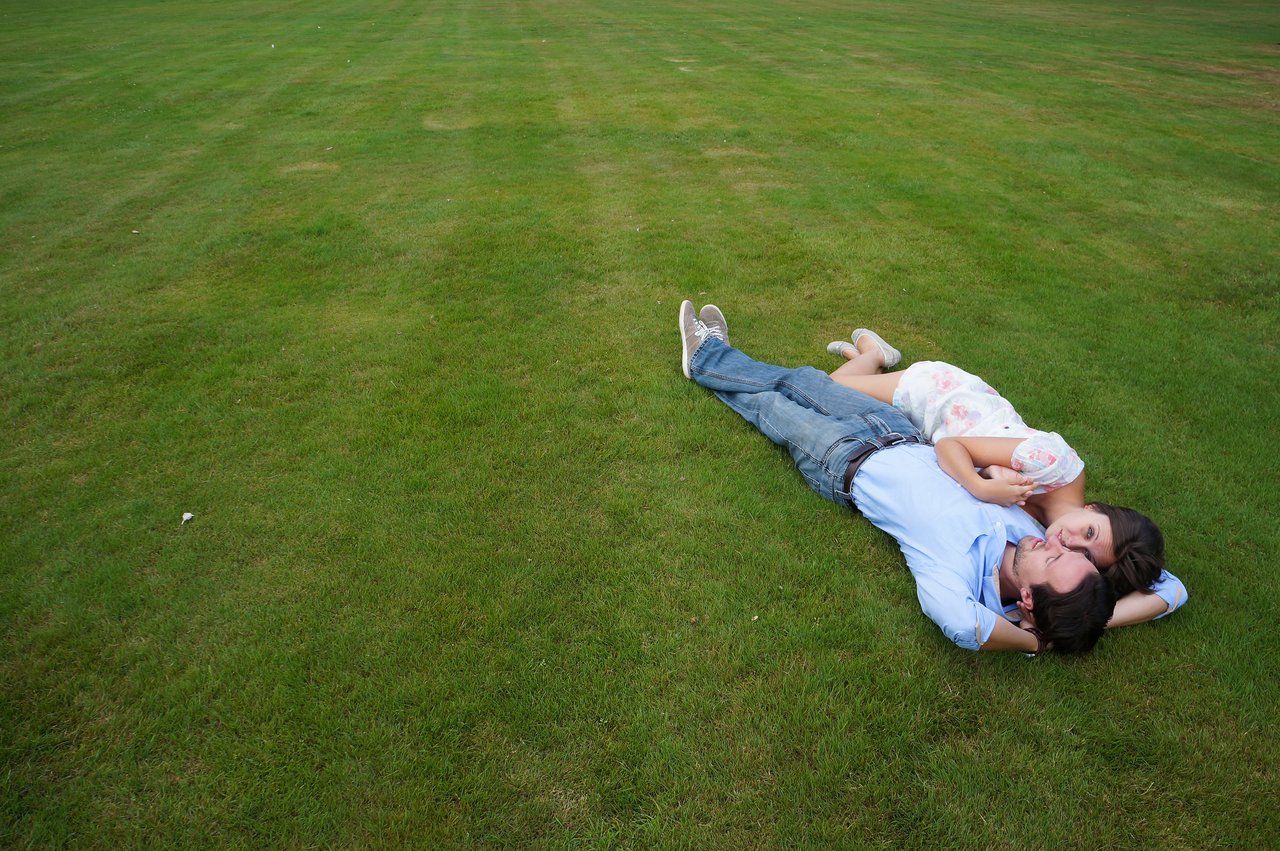 A couple lies on the grass, embracing and looking at each other closely.