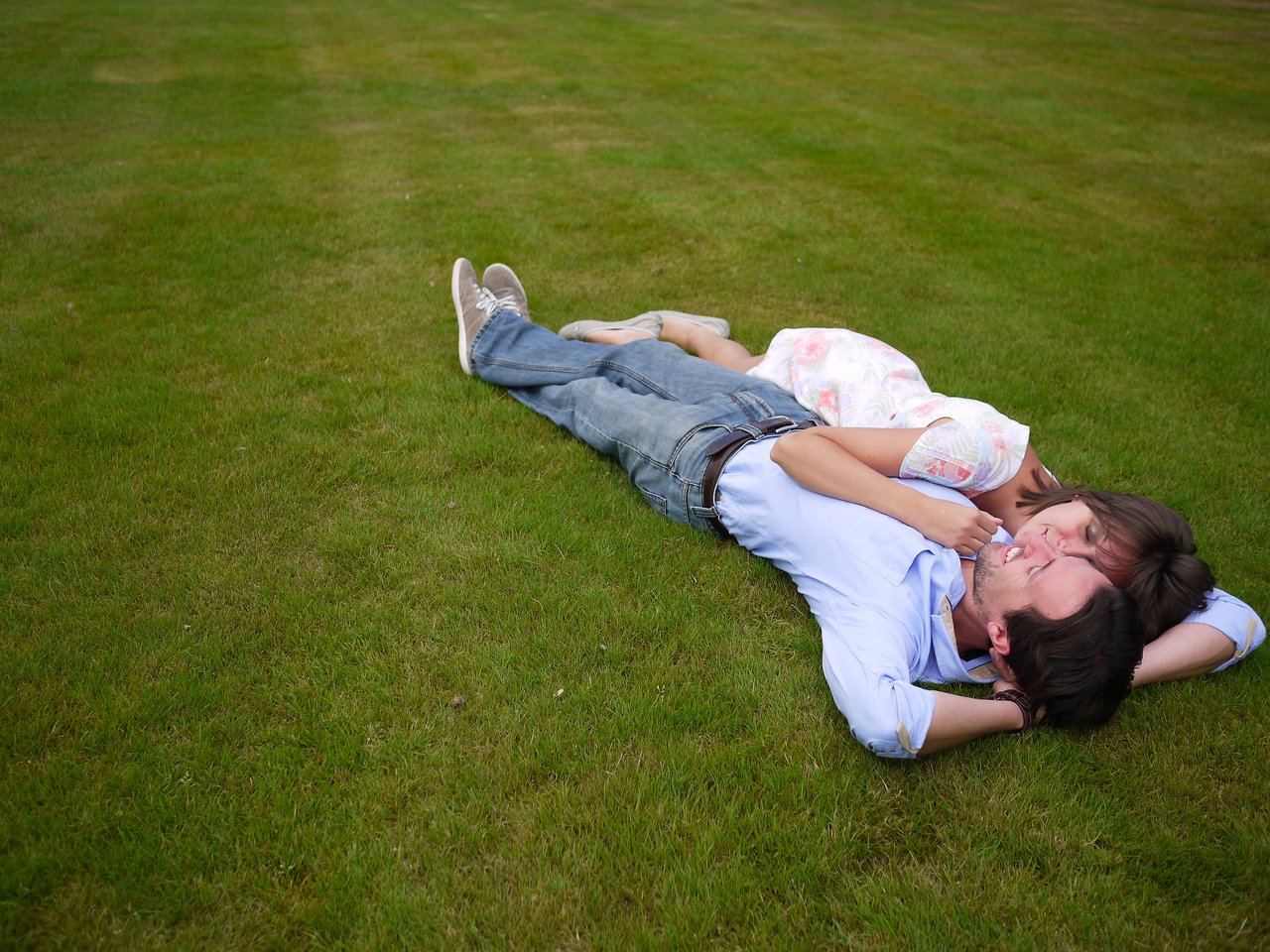 A couple lies on the grass, smiling and embracing each other closely.