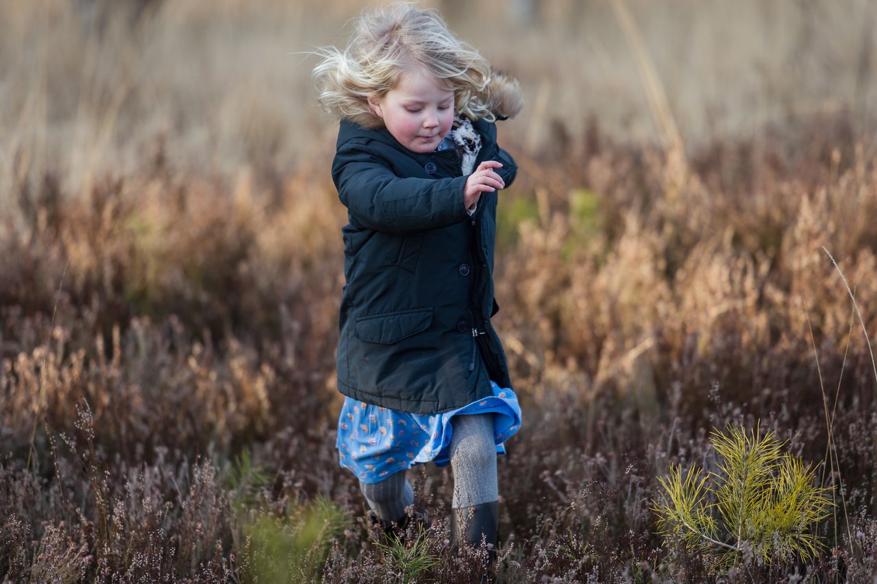 A young child in a black coat runs through a field of tall, dry grass.