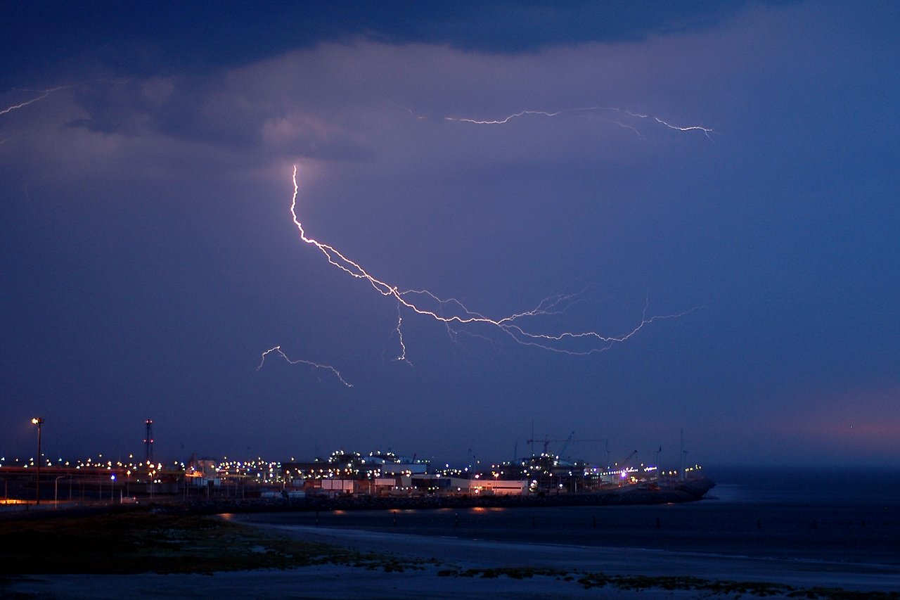 Lightning bolts flash across the dark sky above a brightly lit gas terminal at the Port of Zeebrugge.