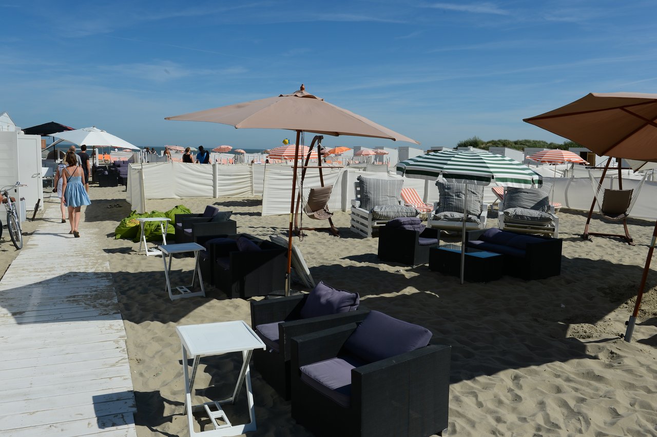 Outdoor beach lounge with cushioned chairs, umbrellas, and sunbeds on the sand.