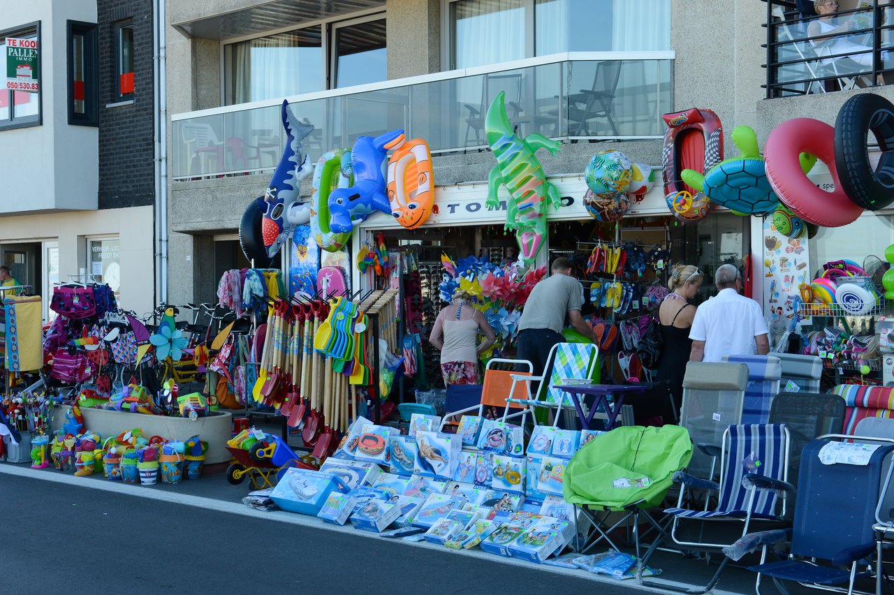 A shop displays colorful beach toys, inflatables, and chairs while people browse the selection outside.