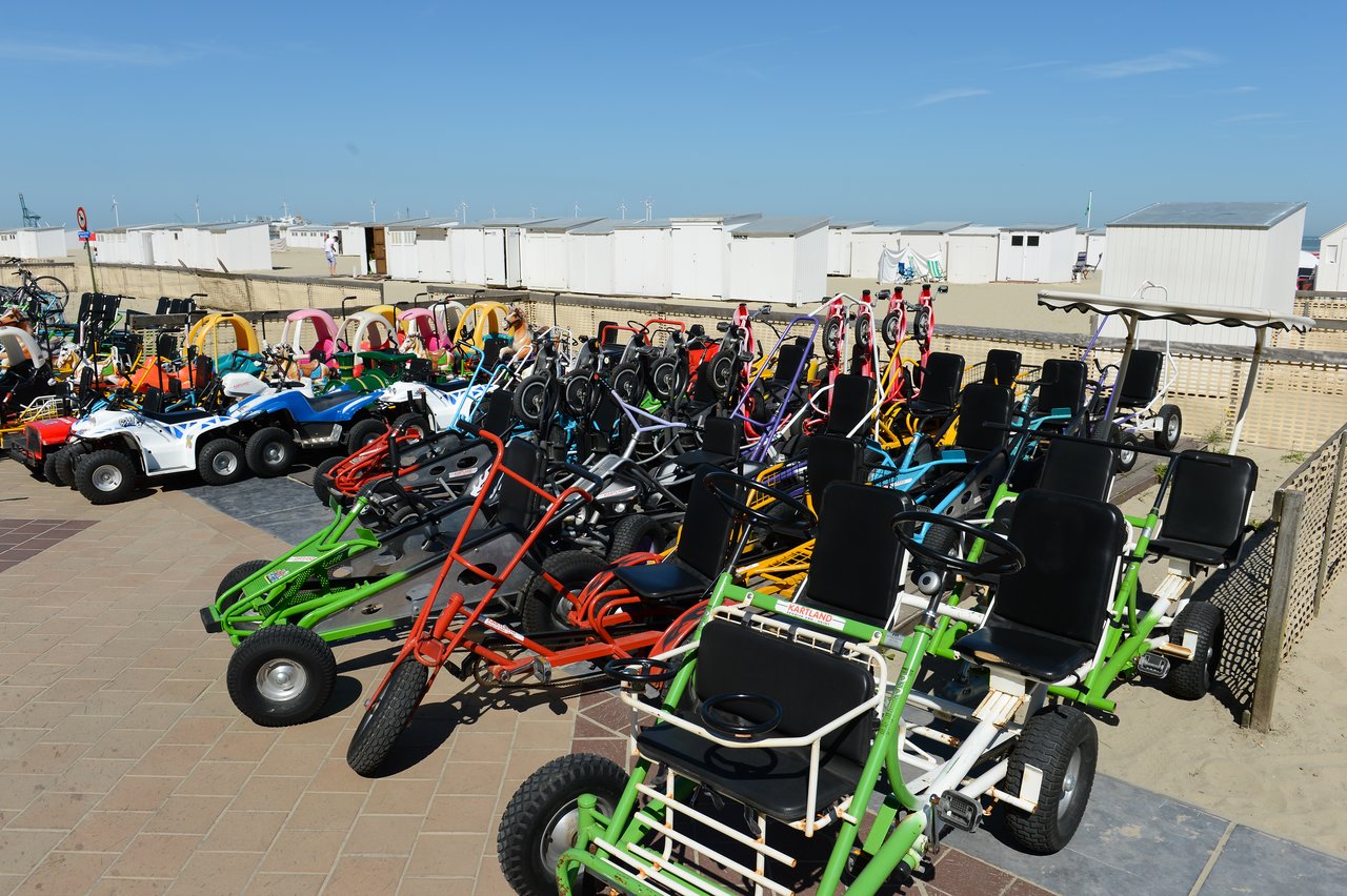 Rows of colorful go-karts parked on a paved area near the beach, ready for rental or use.