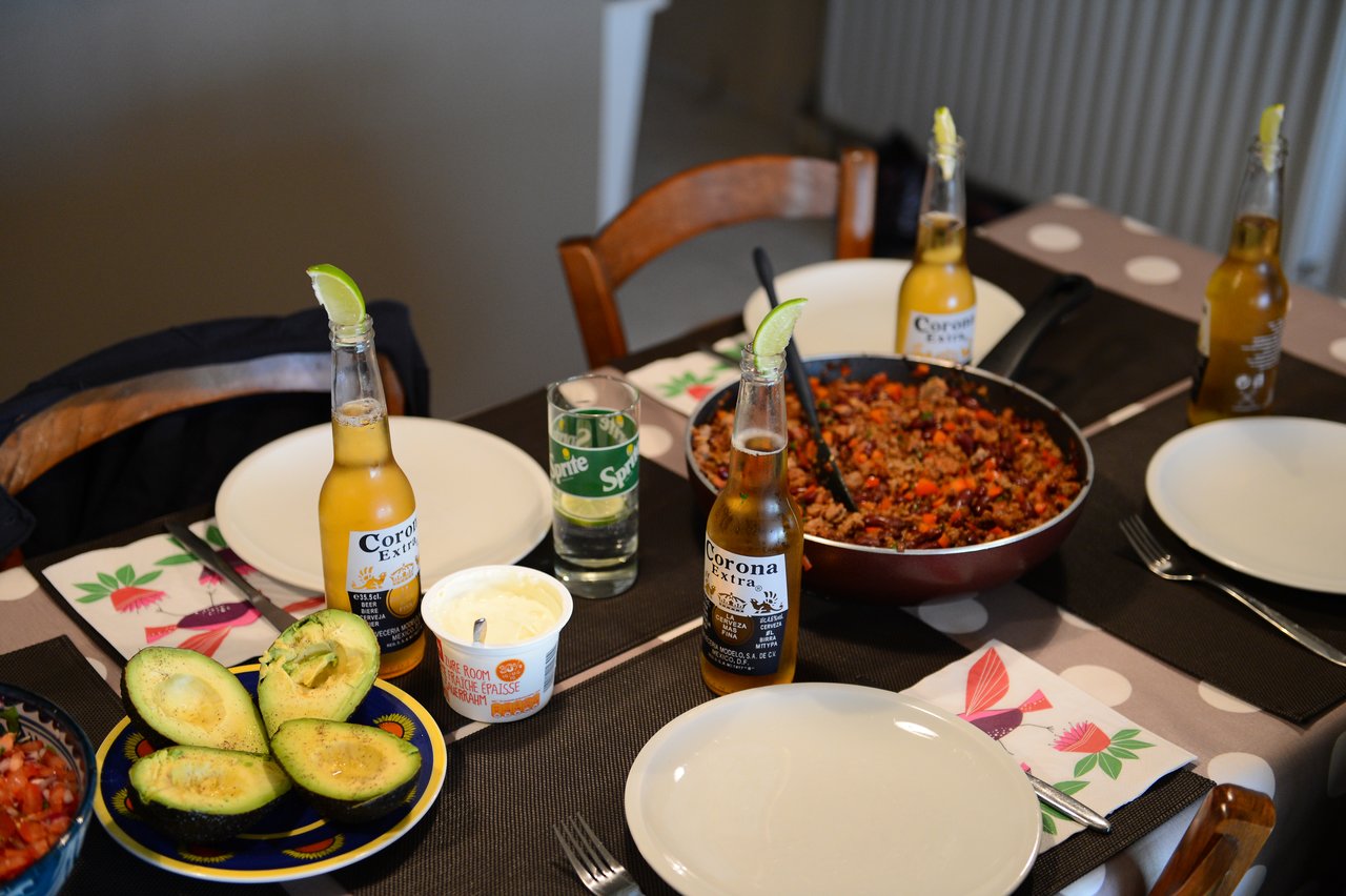 A table set for a Mexican dinner with avocados, a pan of seasoned meat, and bottles of Corona beer.