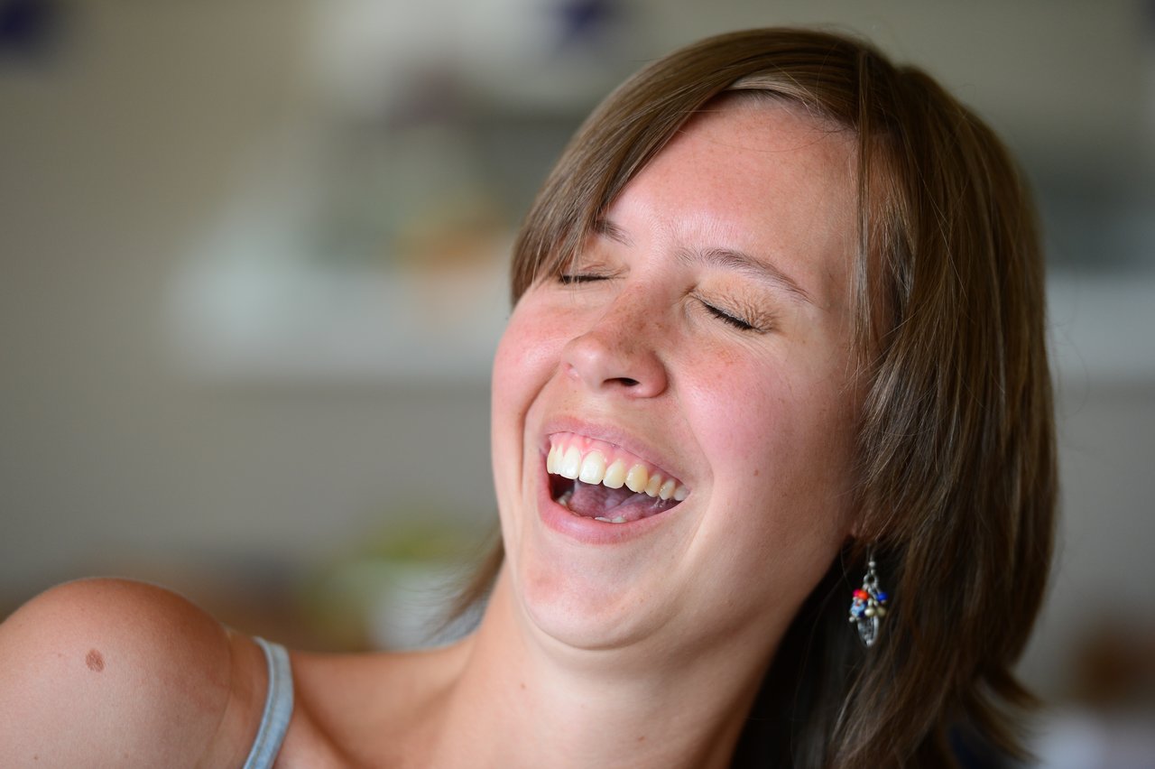 A woman with short brown hair laughs with her eyes closed, showing her teeth.