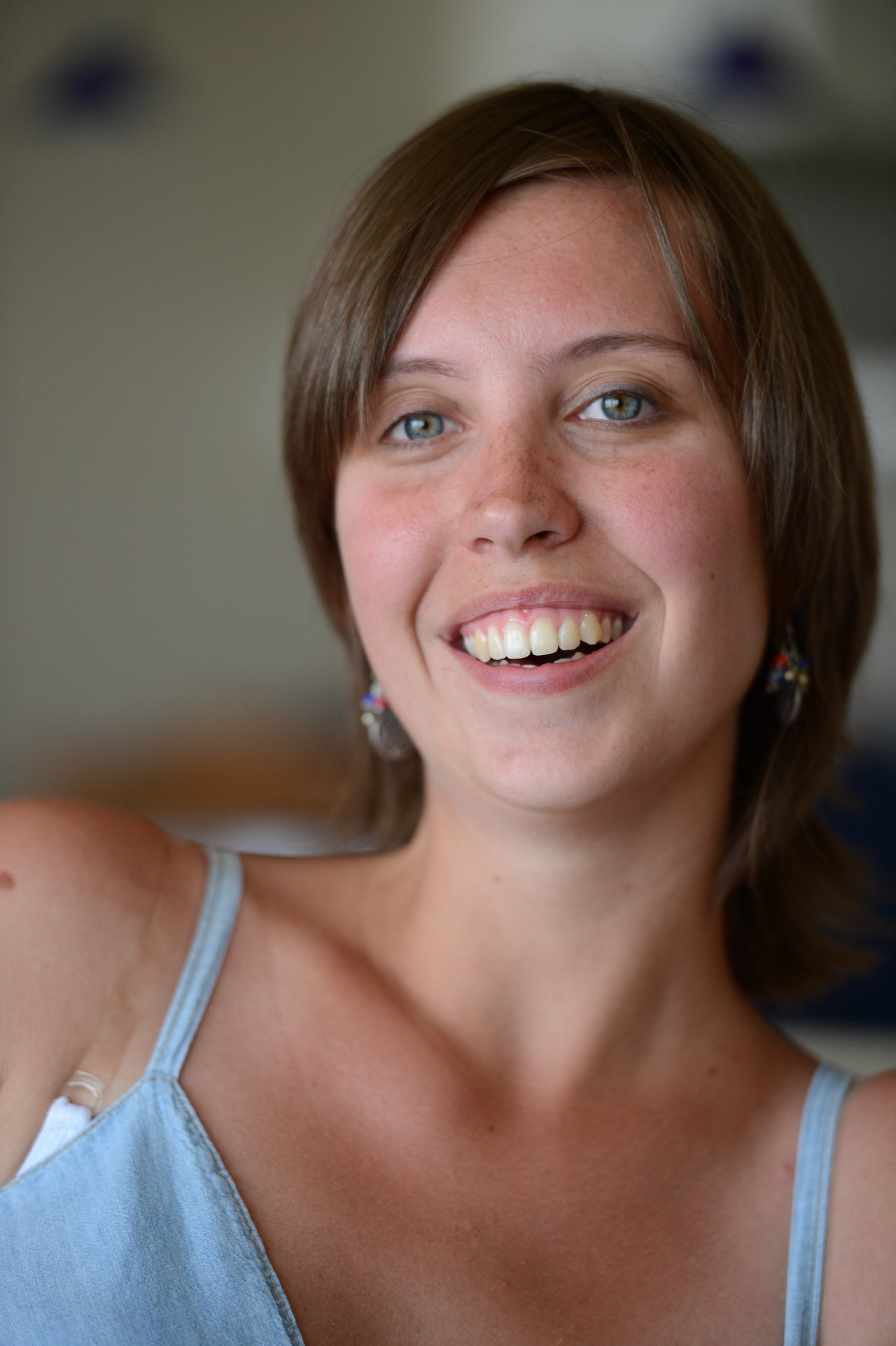 A woman with short brown hair and earrings smiles while looking slightly past the camera.