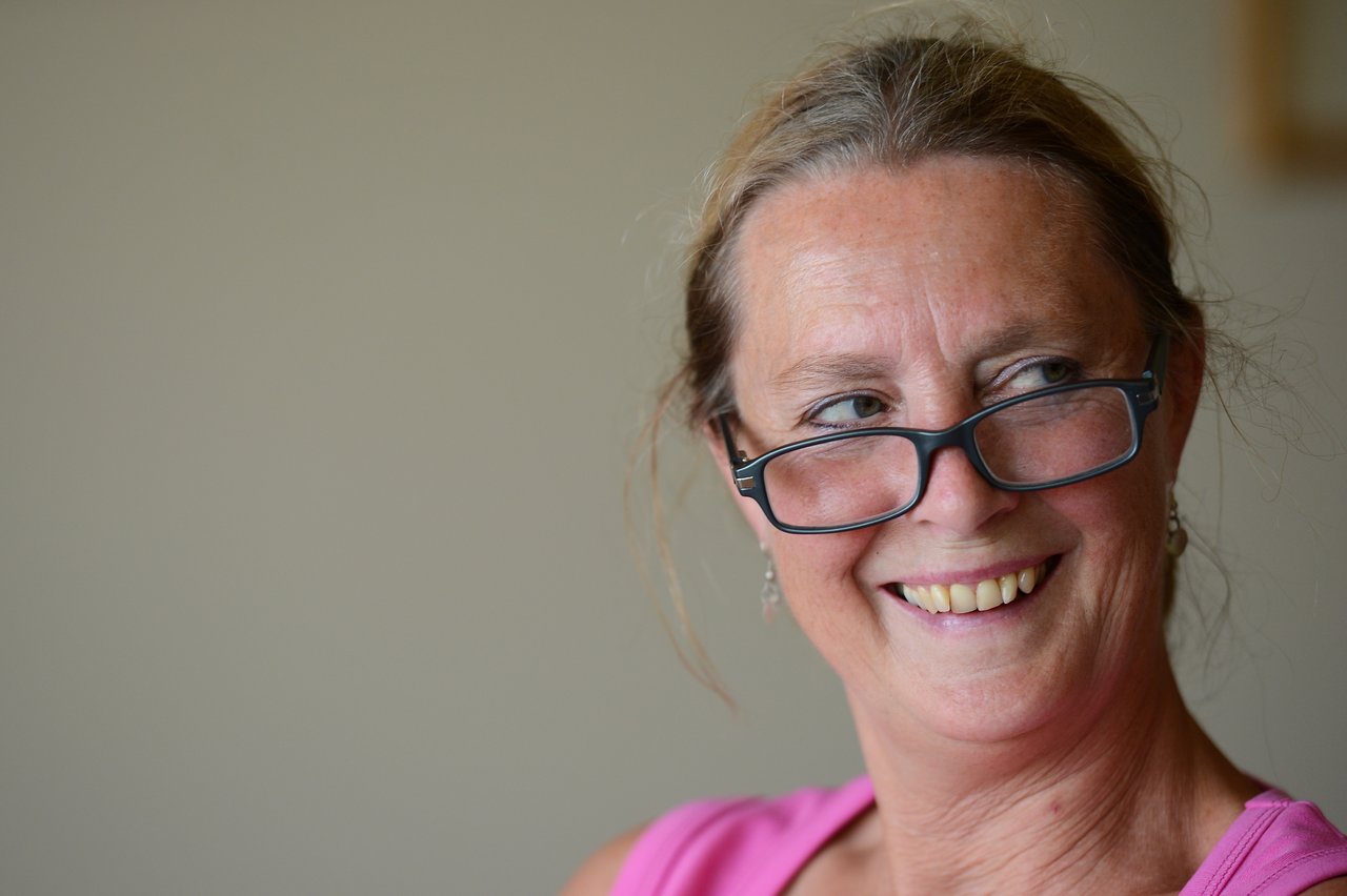 A woman in a pink top smiles while wearing glasses slightly lowered on her nose.
