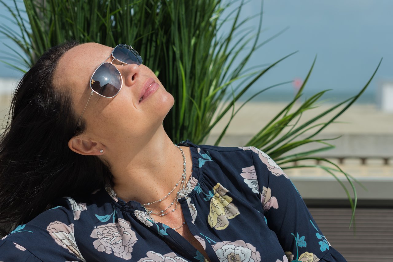 A woman wearing sunglasses tilts her head back and smiles while enjoying the sunlight.