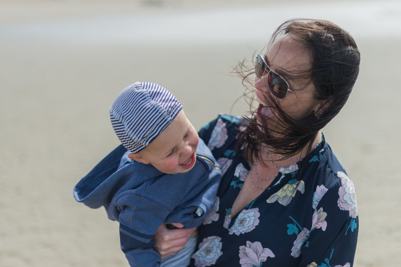 A woman holds a laughing child in her arms while the wind blows her hair across her face.
