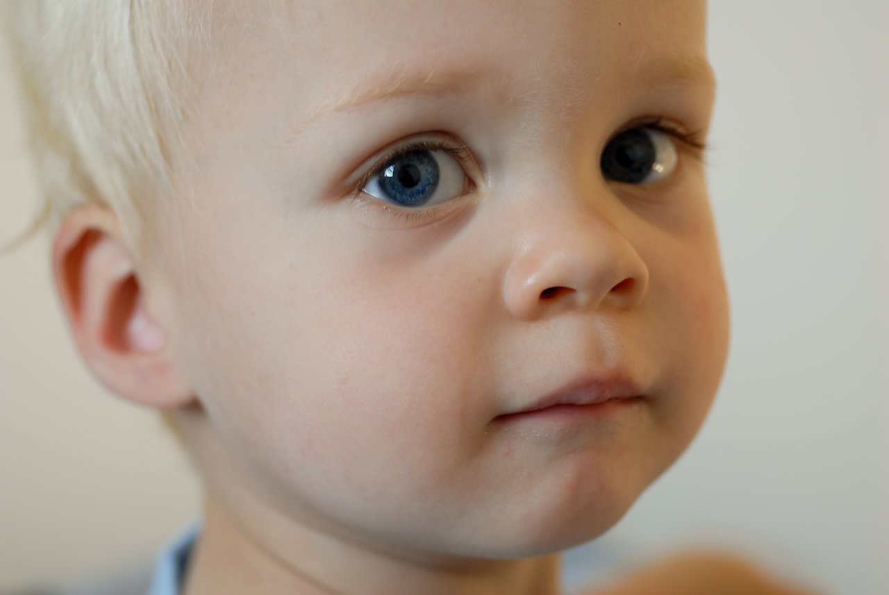 Close-up of a young child with blue eyes and blonde hair, looking slightly to the side with a neutral expression.