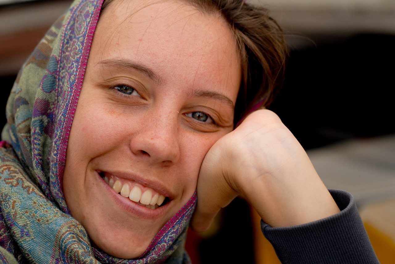 A person wearing a colorful scarf smiles while resting their head on their hand.