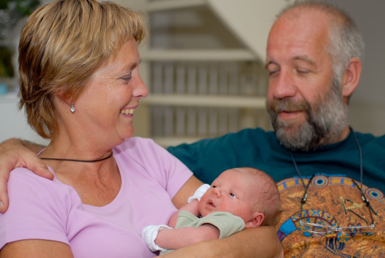 An older couple smiles while holding a newborn baby in their arms.