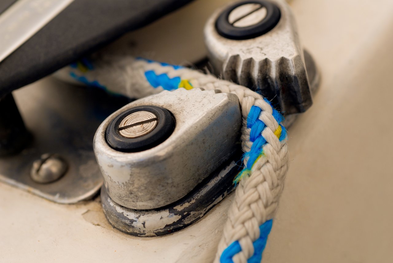 Close-up of a sailing rope secured in a metal cam cleat on a boat.