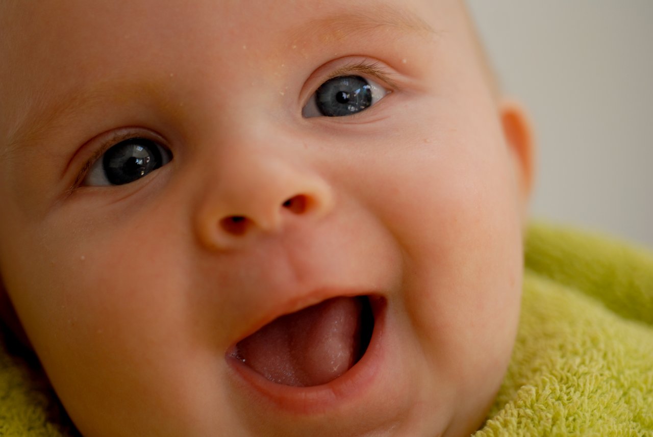 Close-up of a baby with bright eyes and an open mouth, wrapped in a green towel.