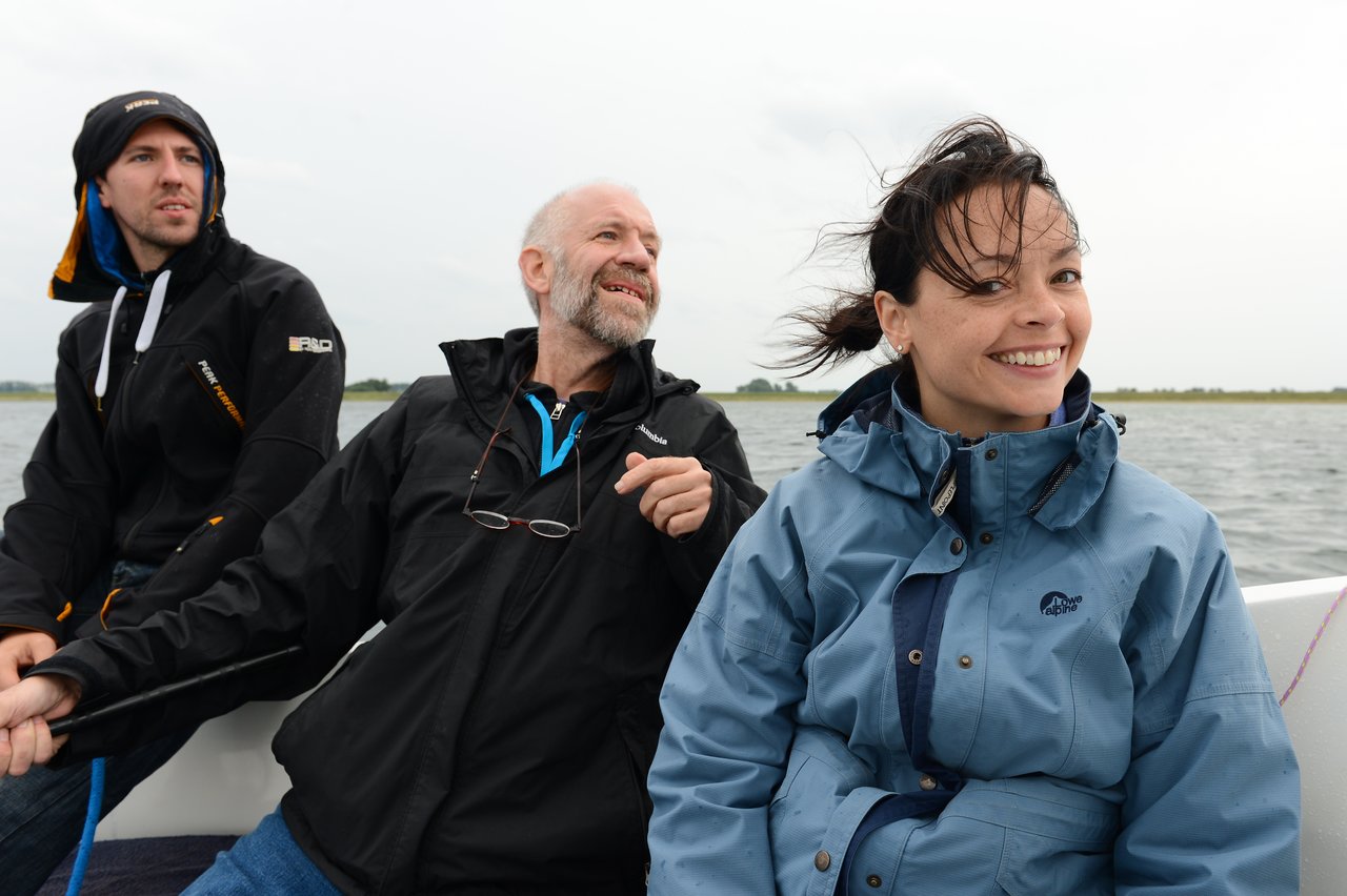 Three people in jackets are on a boat, smiling and looking in different directions as they enjoy the ride.