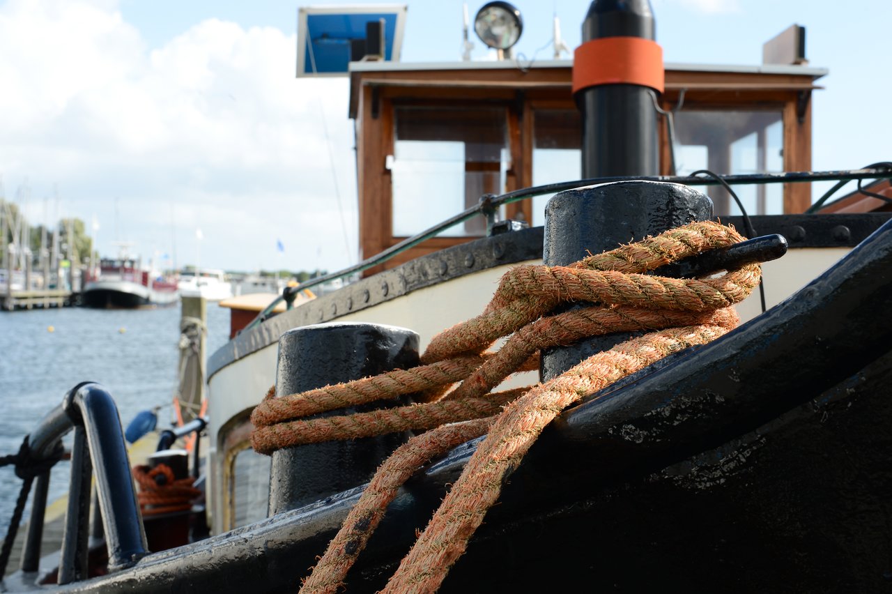 A thick rope is tightly wrapped around a metal post on the bow of a boat in a harbor.
