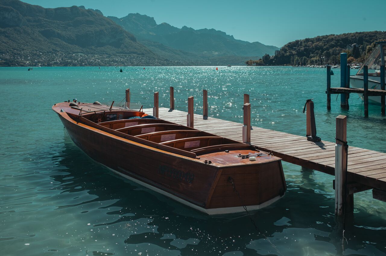 Wooden boat tied to a dock on Lake Annecy, resting in calm water on a sunny day.