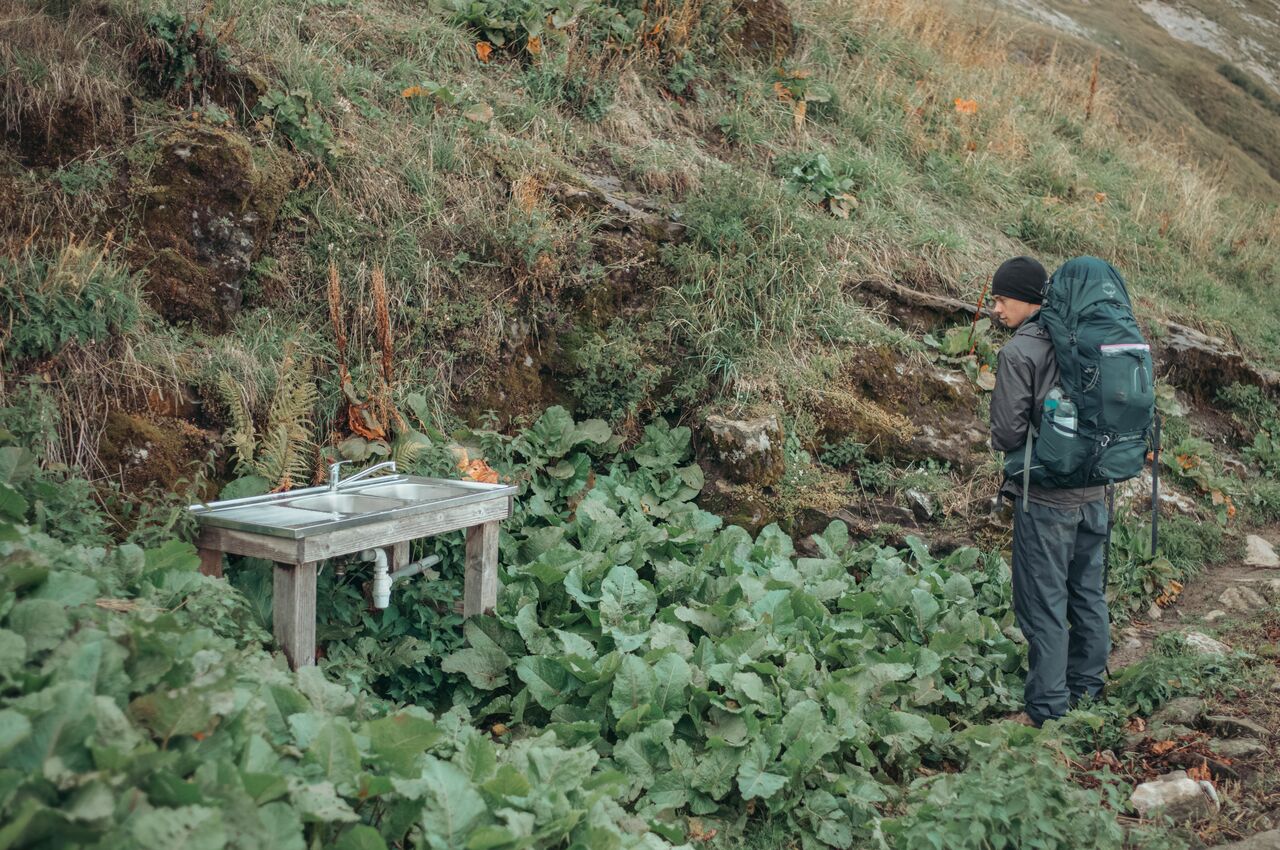 Outdoor sink at Refuge de Praz D'zeures where a backpacker refills water bottles during a mountain hike.