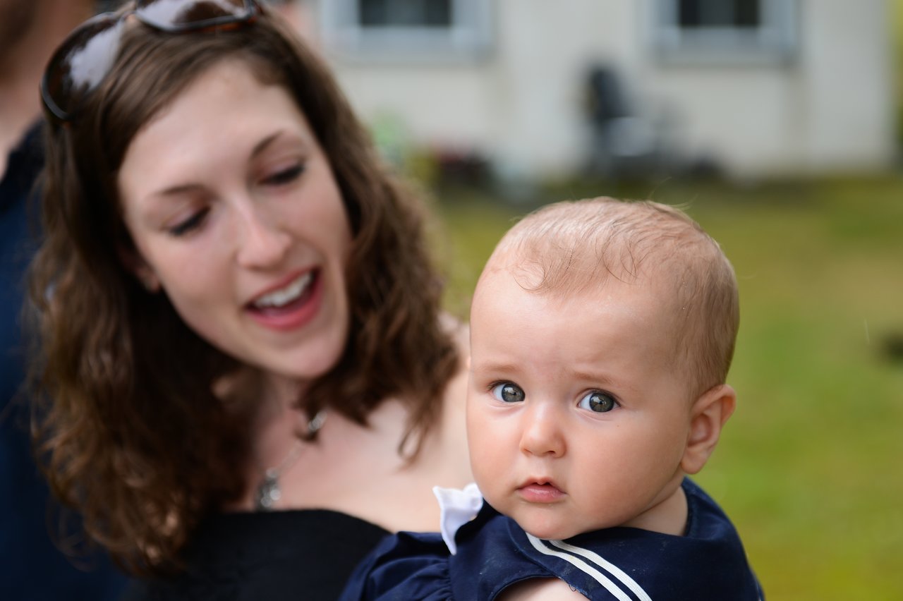 A woman holds a baby who looks directly at the camera with a curious expression.