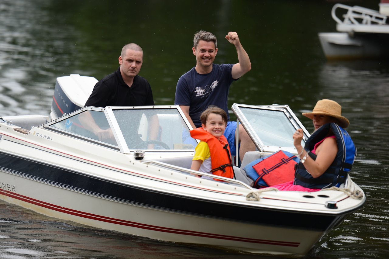 A group of four people on a small motorboat, smiling and wearing life jackets on the water.