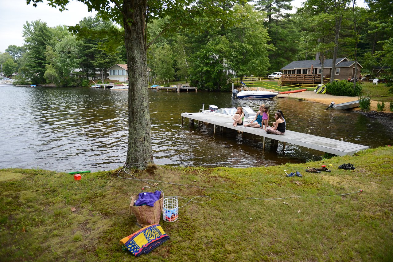 Three people and a child sit on a dock by the lake, talking and relaxing near the water.