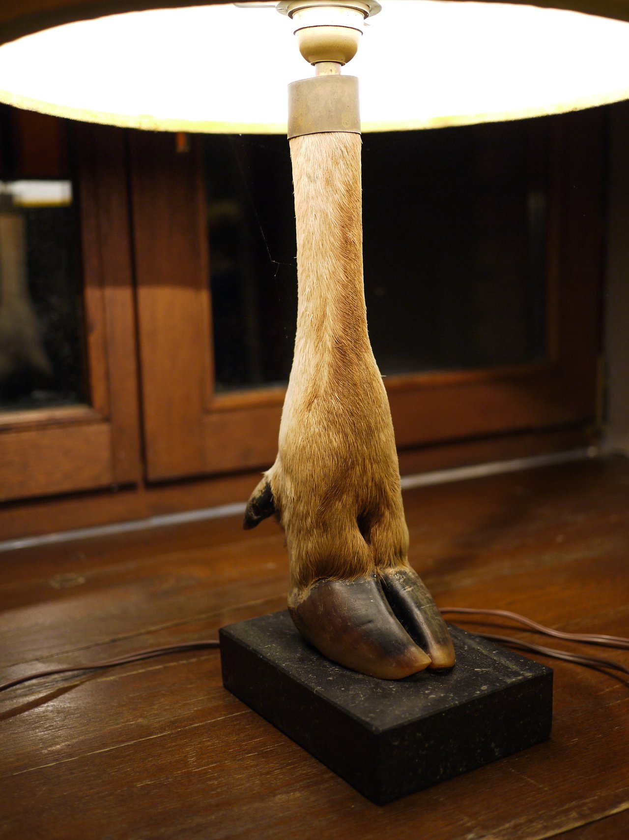 A table lamp with a base made from a taxidermy animal leg and hoof, placed on a wooden surface.