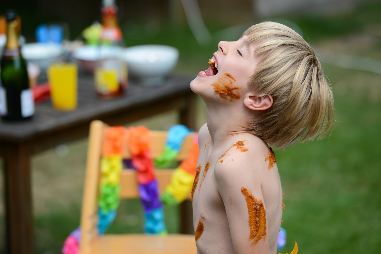 A child with food smeared on their skin laughs with their mouth open at an outdoor celebration.
