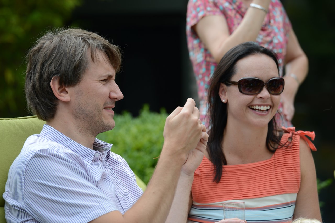 A man and a woman are sitting outdoors, smiling and talking.