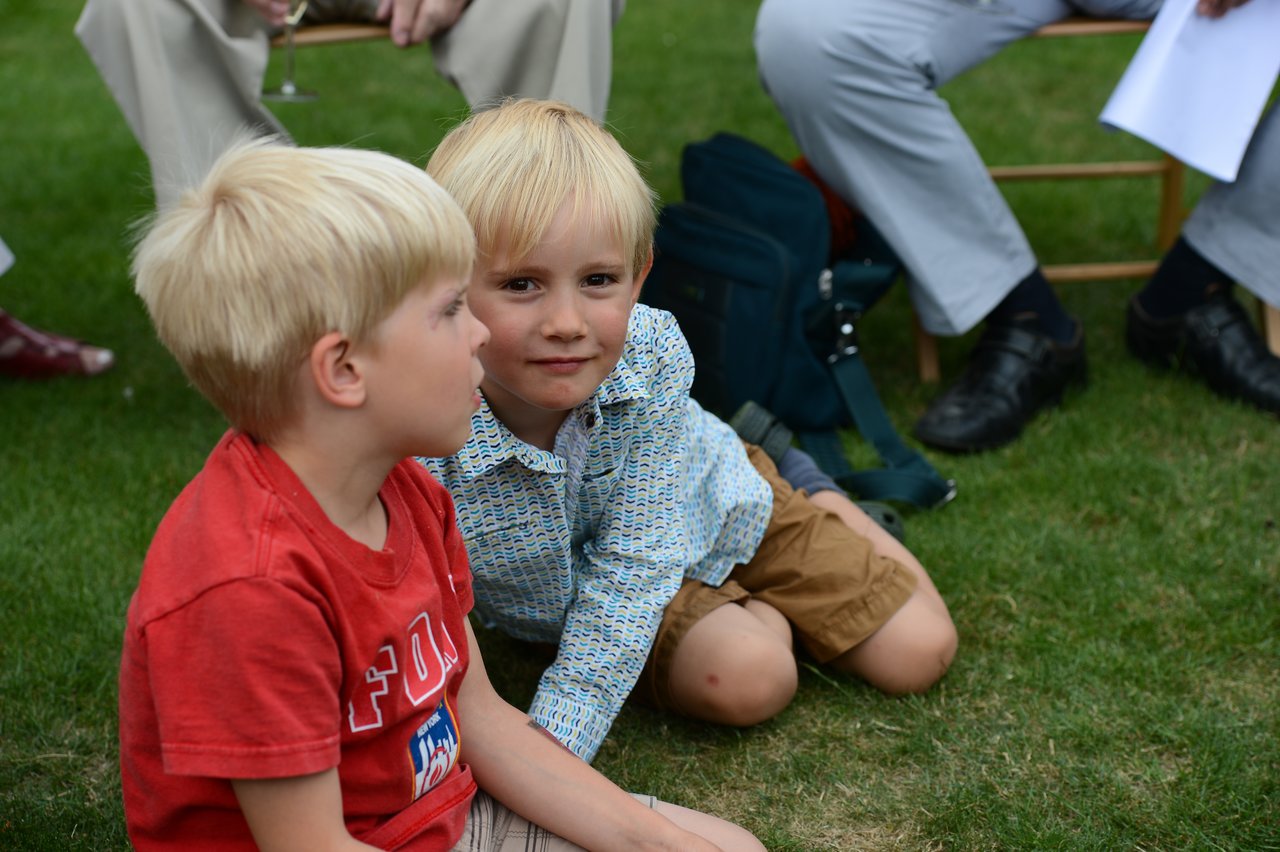 Two young boys sit on the grass, one looking at the camera while the other faces away.