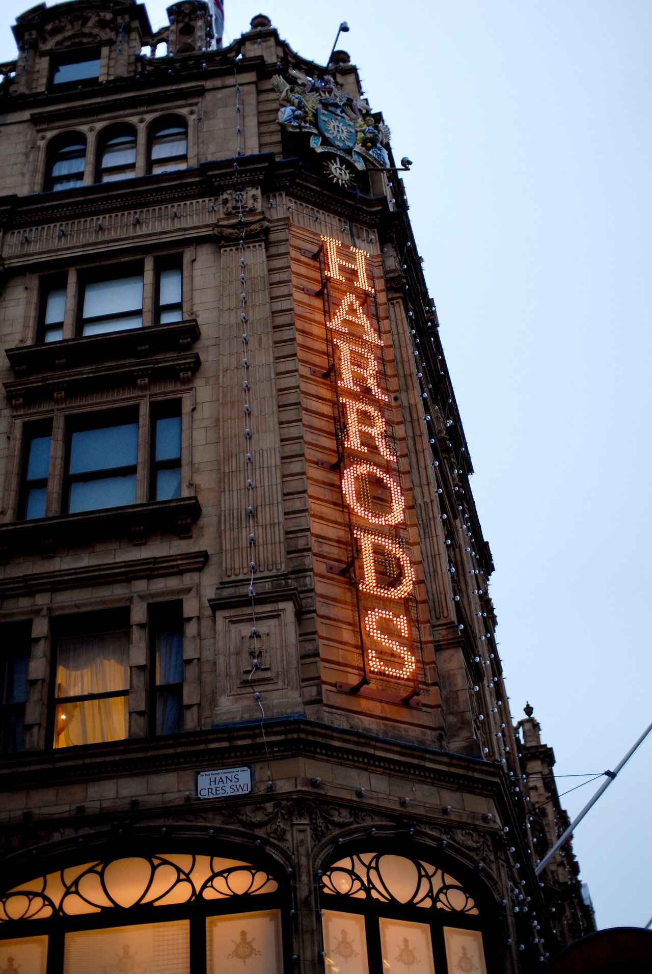 The exterior of Harrods department store with its illuminated sign on a historic building in London.