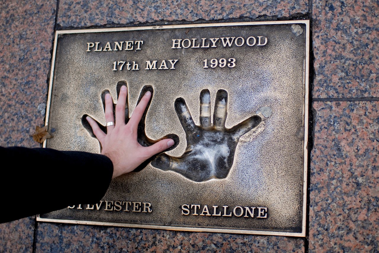 A person places their hand on Sylvester Stallone's handprint plaque at Planet Hollywood, dated May 17, 1993.