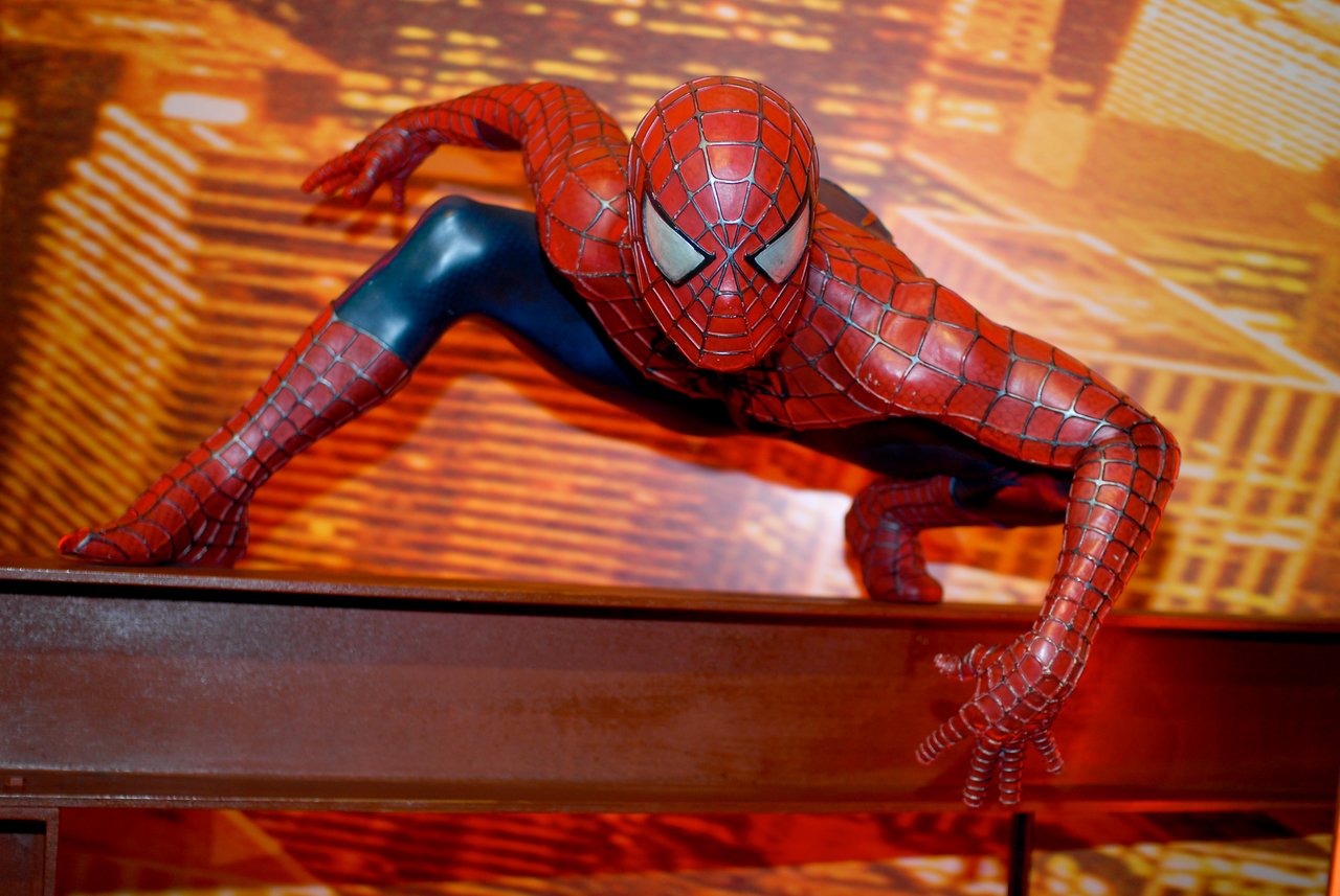 A statue of Spider-Man crouching on a ledge, posed as if ready to leap, with a city backdrop.