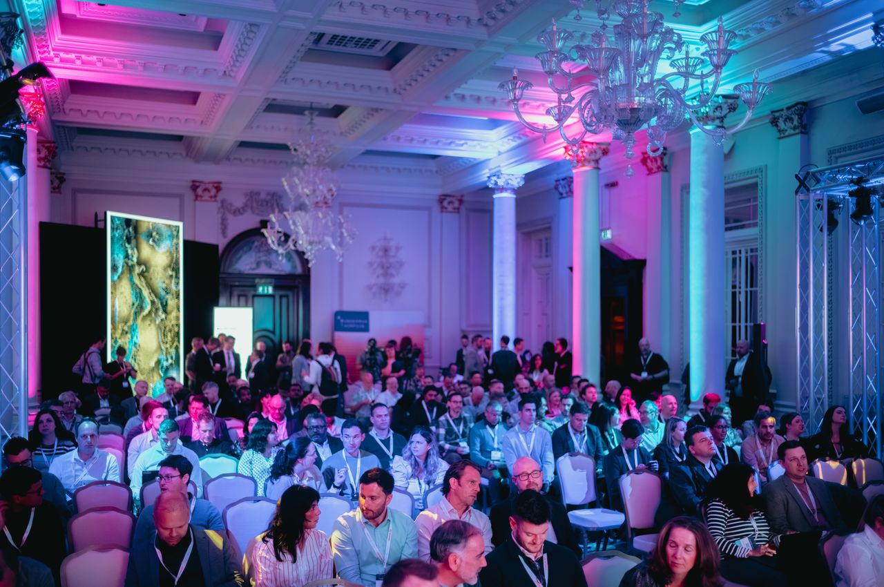 A view of a grand ballroom filled with conference attendees waiting for presentations to start.
