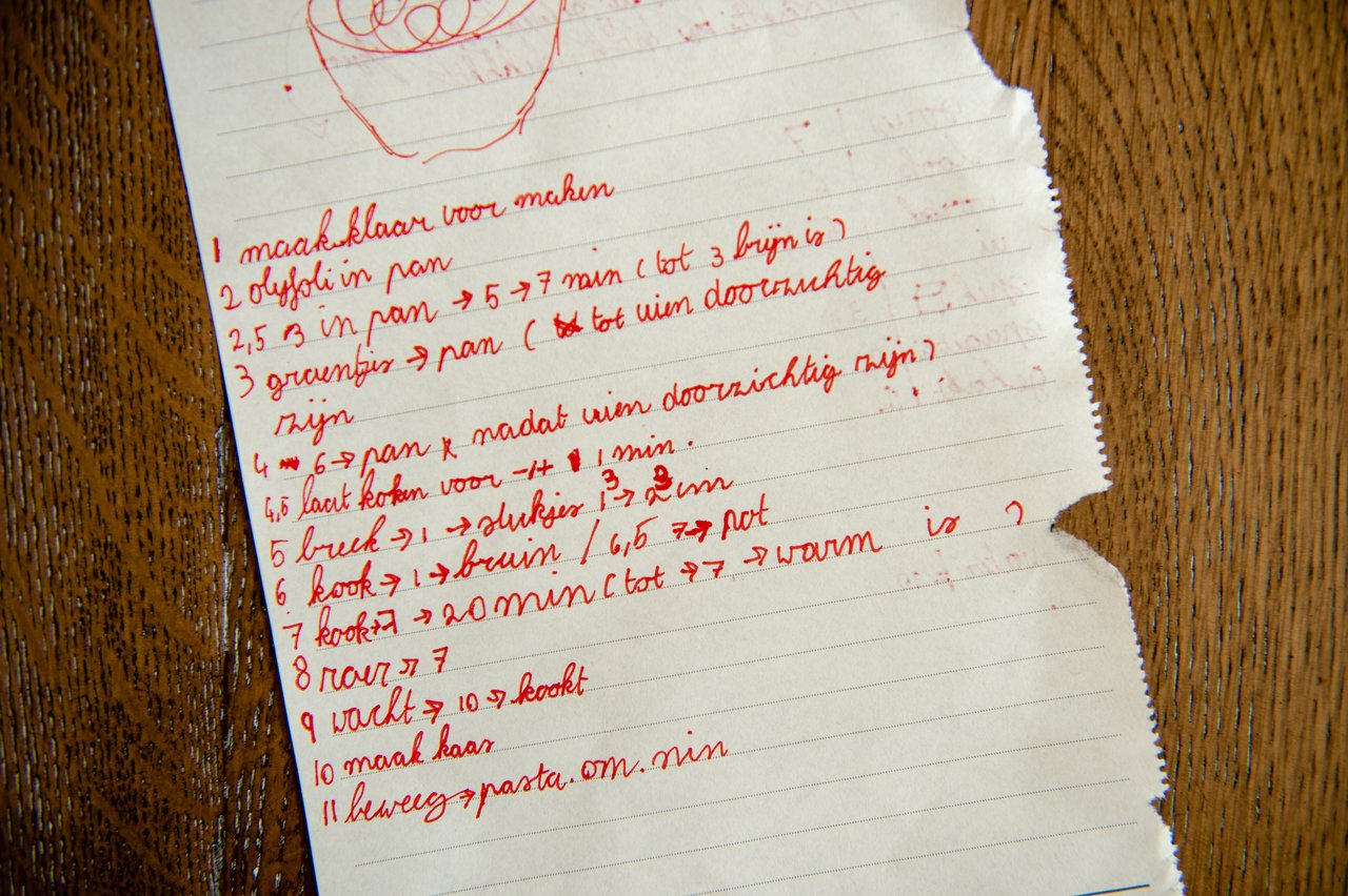 A handwritten recipe in red ink on torn lined paper, listing numbered cooking steps in Dutch.