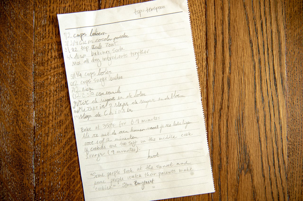 A handwritten cookie recipe on lined paper rests on a wooden table.