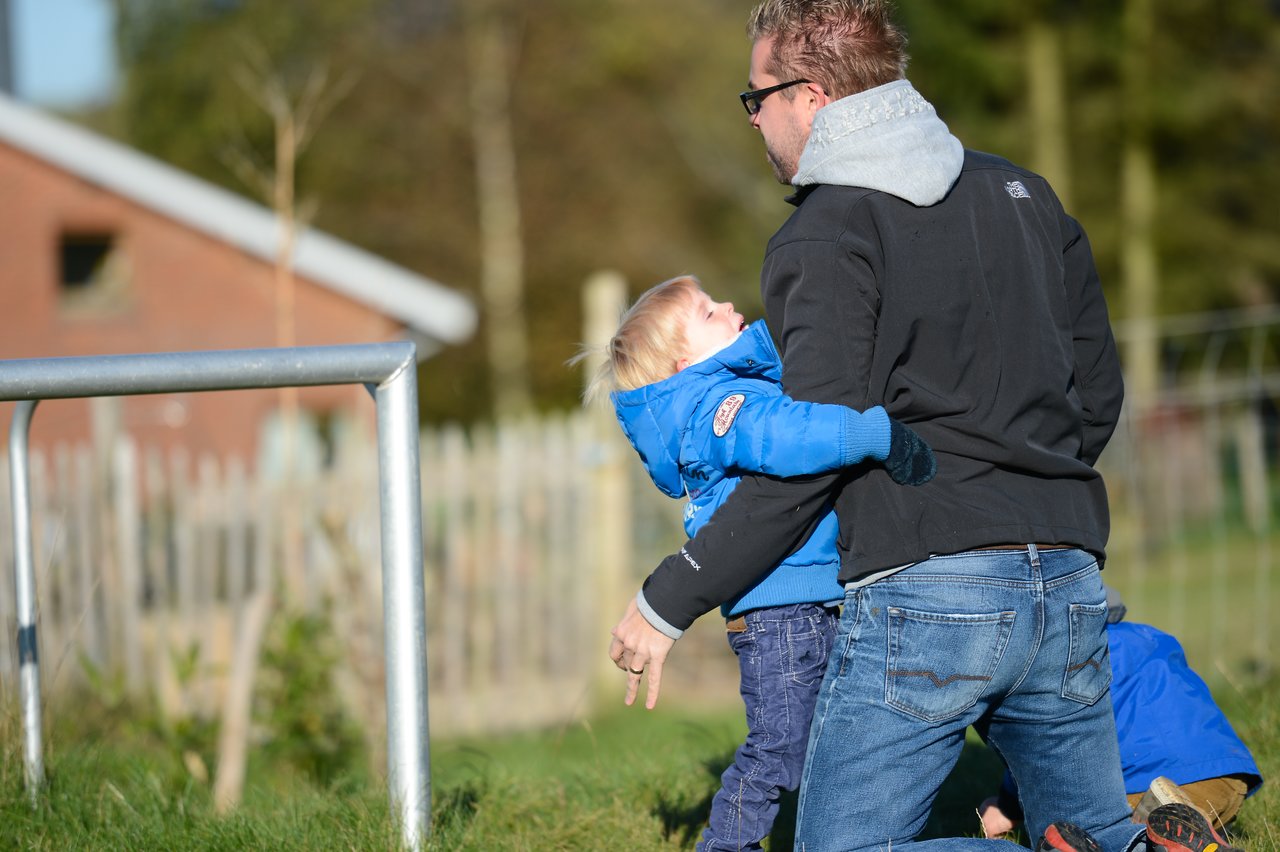 A man in a black jacket holds a child in a blue coat while another child is on the ground.