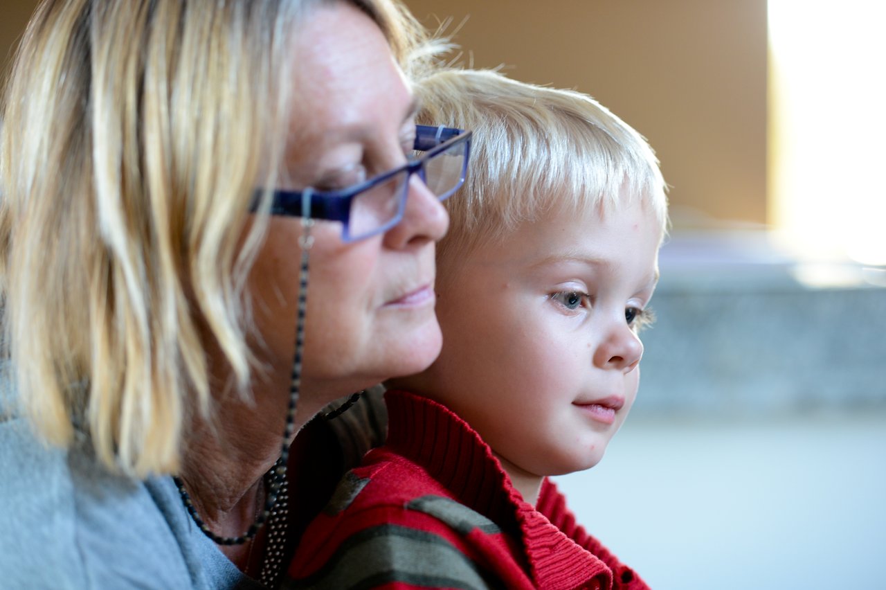 A woman wearing glasses sits closely with a young child, both looking intently at something off-camera.