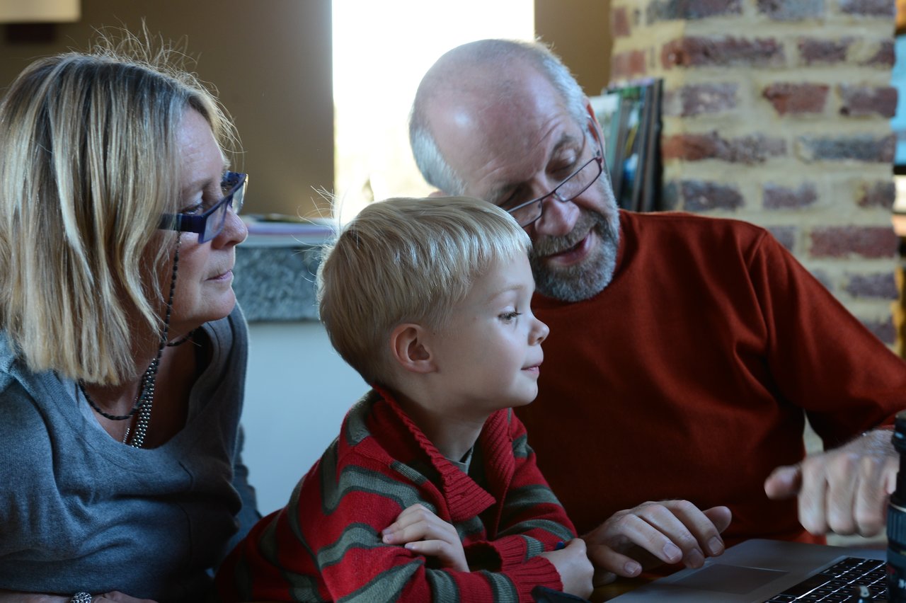 An older man, a woman, and a young boy look at a laptop screen together, engaged in discussion.