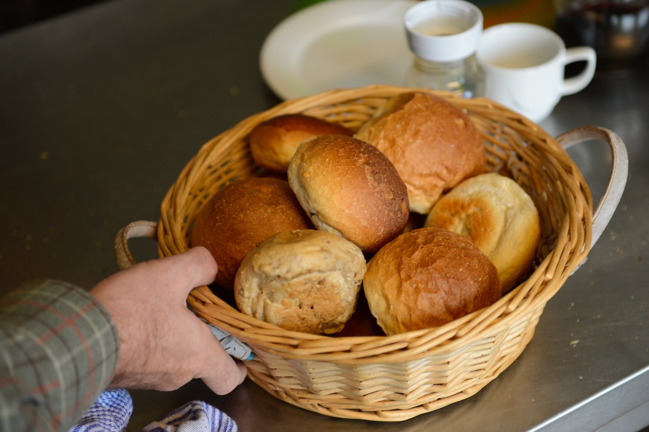 A person reaches for a wicker basket filled with assorted bread rolls on a kitchen counter.
