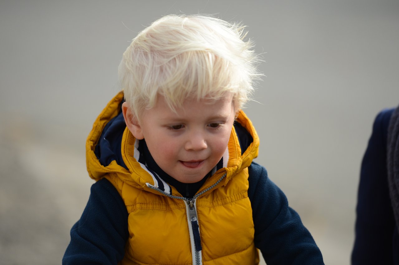 A young child with blond hair and a yellow vest looks down with a focused expression.