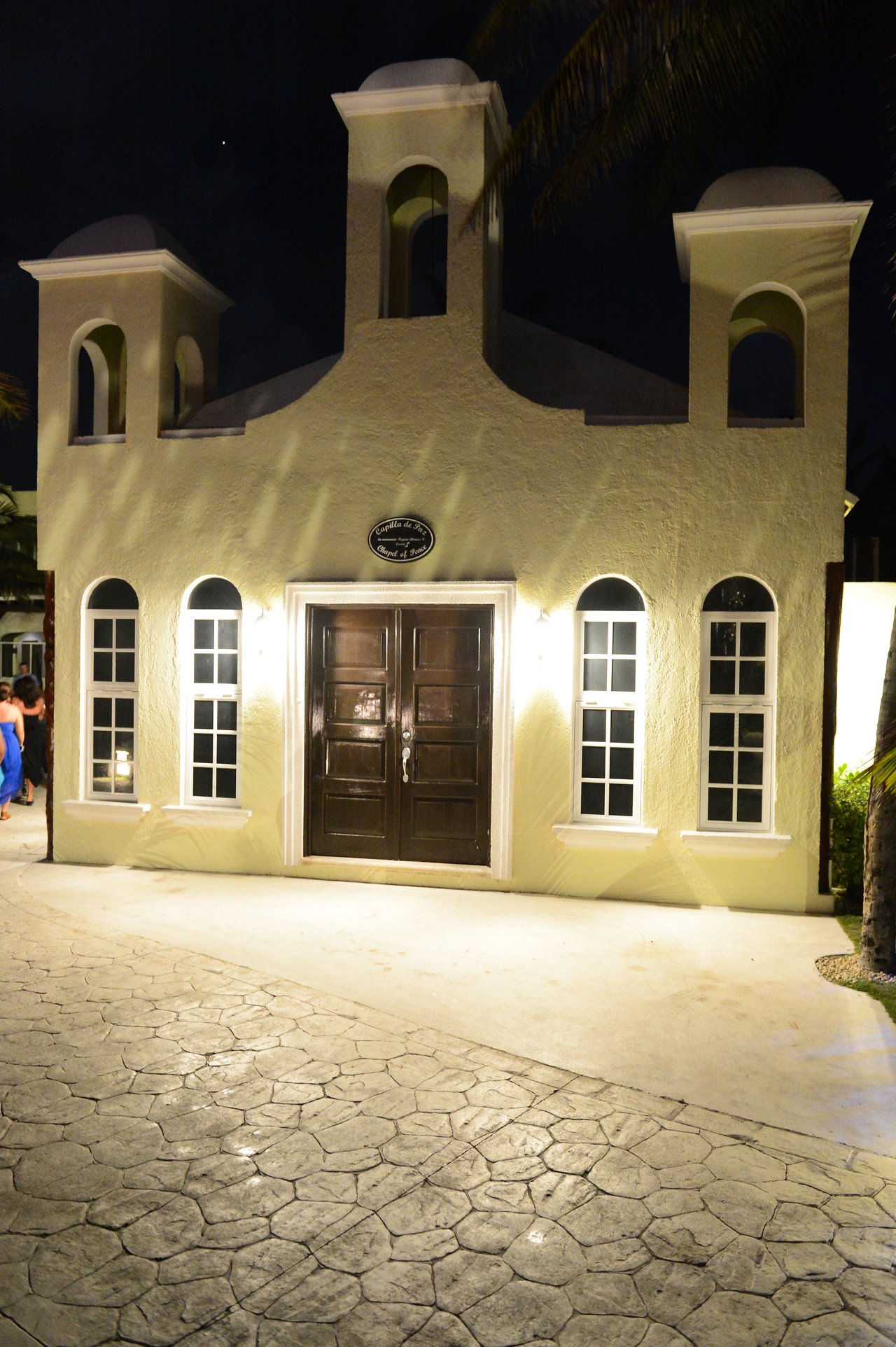 A small, well-lit chapel with a beige facade and dark wooden doors at night in Cancun.
