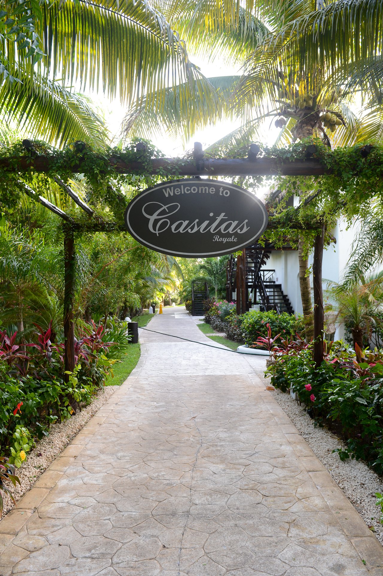 A stone pathway leads through a tropical resort entrance with a sign reading "Welcome to Casitas Royale.