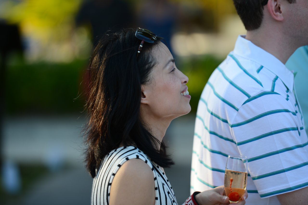 A woman in a striped dress smiles while holding a glass of champagne with a cherry inside.