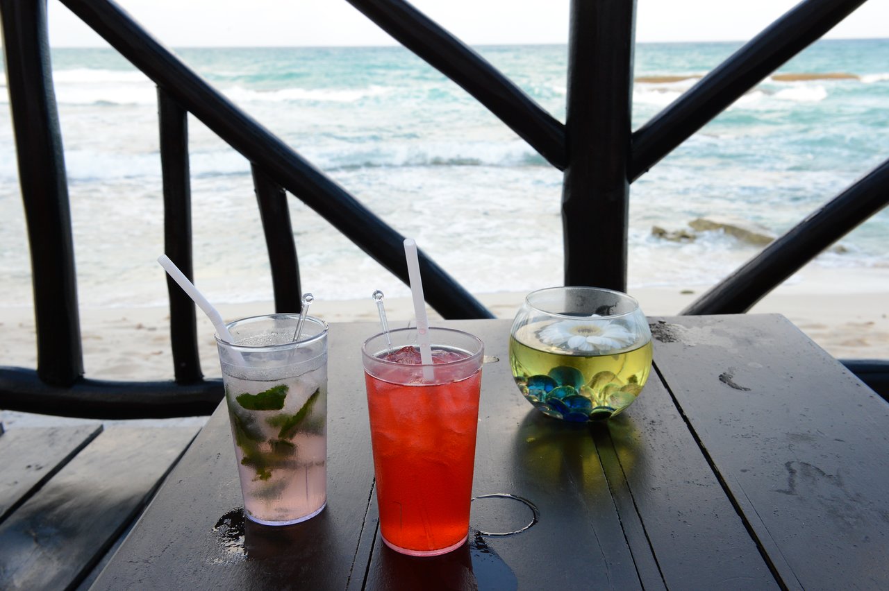Two colorful drinks and a small decorative bowl on a wooden table overlooking the ocean in Cancun.